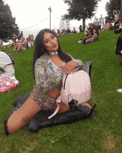 Woman sitting on grass with a pink backpack at an outdoor event