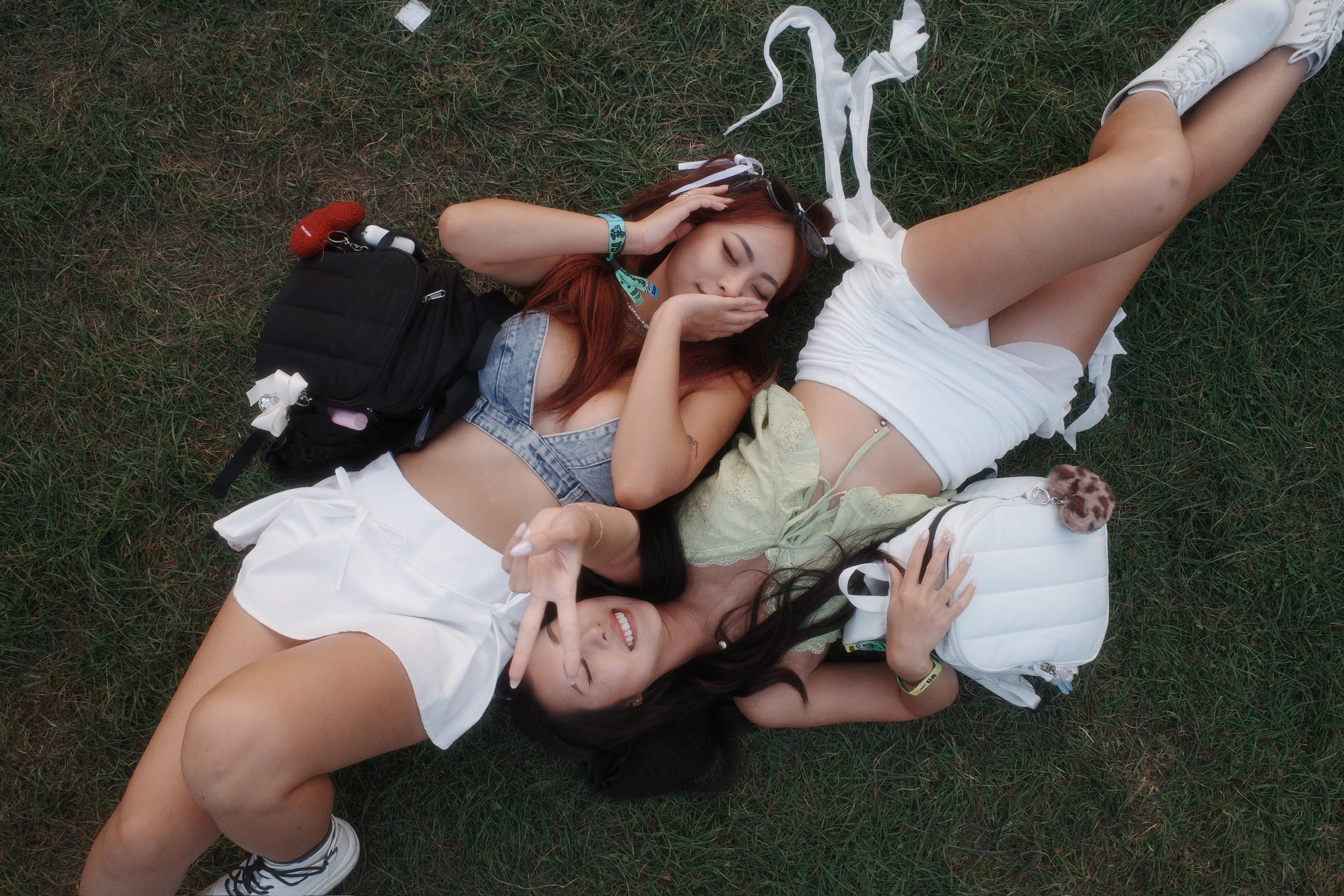 Two people lying on the grass with a backpack and shoes around them.